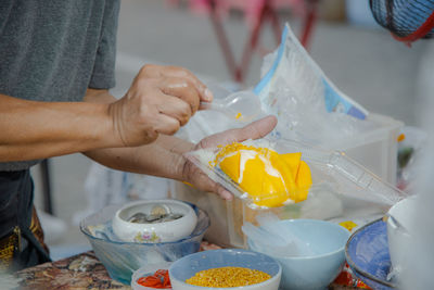 Close up hand making mango sticky rice with coconut milk at street food market.