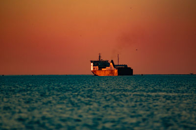 Boat sailing on sea against orange sky