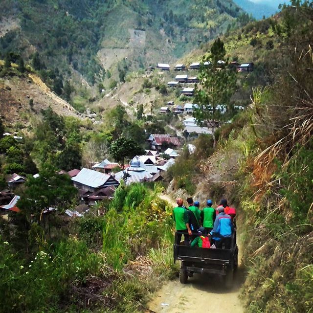 building exterior, green color, high angle view, built structure, house, architecture, grass, land vehicle, village, mountain, transportation, day, tree, car, residential structure, outdoors, plant, mode of transport, landscape