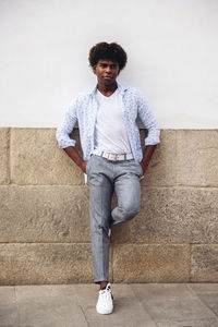 Determined african american male in trendy outfit and with afro hairstyle leaning on stone wall of building and looking away