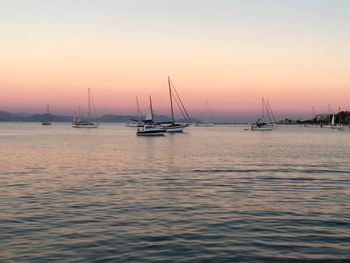 Boats sailing in sea at sunset