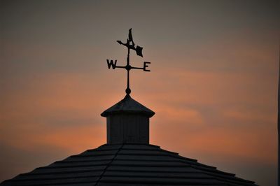 Low angle view of weather vane on building against cloudy sky during sunset