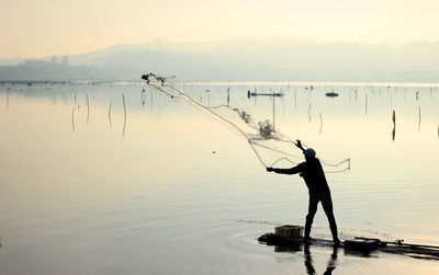 Man fishing in lake against sky during sunset