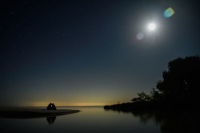 Silhouette trees by lake against sky at night