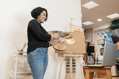 Smiling female artist on video call through laptop holding palette at studio