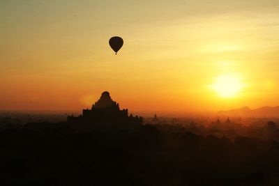 Silhouette hot air balloon over pagodas against sky during sunset