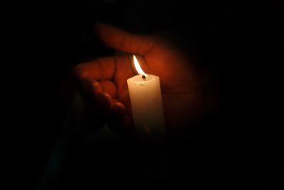 Close-up of hand holding lit candle in darkroom