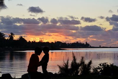 Silhouette kid and mom looking at lake against sky during sunset