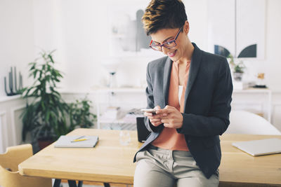 Happy businesswoman using mobile phone while standing at table in office