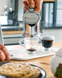 Man preparing classic italian coffee mocha, pouring coffee from moka pot into glass coffee cup.