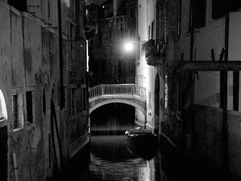 Arch bridge over canal amidst buildings at night