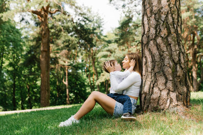 Mom and her son have fun spending family weekends in the park in summer, sitting near a tree