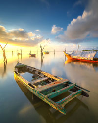 Fishing boats moored in sea against sky during sunset