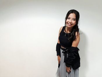 Portrait of smiling young woman with hands in pockets standing against white background