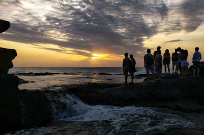 Silhouette people standing on beach against sky during sunset