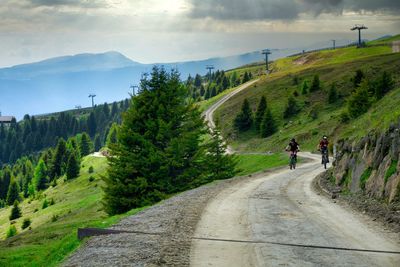 Rear view of people walking on road by mountain against sky