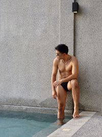 Portrait of shirtless man standing against wall