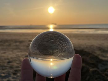 Midsection of person holding crystal ball against sea during sunset