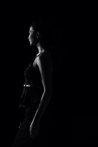 Side view of young woman standing against black background