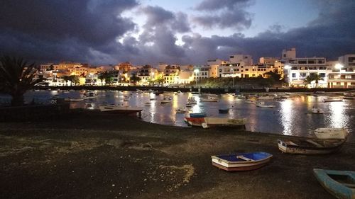 Boats moored in illuminated city against sky at night