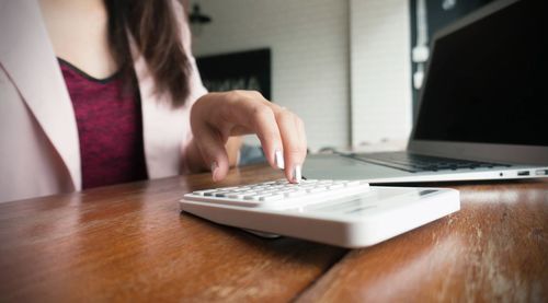 Midsection of businesswoman using calculator with laptop on table at office