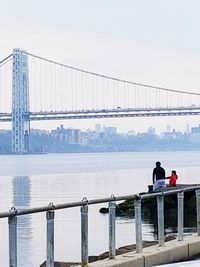 People on bridge over river against sky