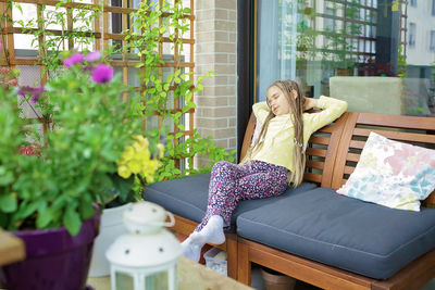 Girl relaxes on balcony at home. wooden table, green plants, sofa, candles. terrace life on vacation