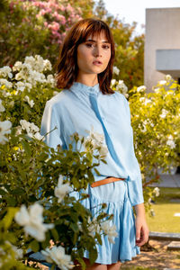 Beautiful young woman standing by flowering plants, wearing a beautiful light blue dress.