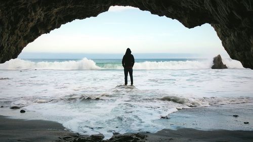 Rear view of man standing on rock looking at horizon