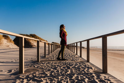 Man standing on railing against clear blue sky