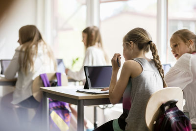 Rear view of girls sitting on desk in classroom