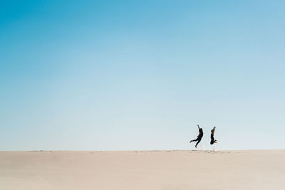 People walking on desert against clear sky