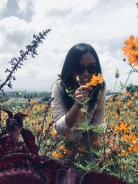 Low section of person holding flowering plant on field against sky