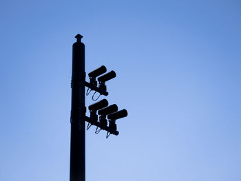 Low angle view of security cameras on pole against clear blue sky