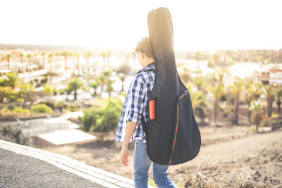 Rear view of boy with guitar walking in city