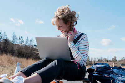 Woman working on a laptop whilst sat on her skateboard outside