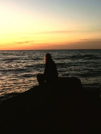 Silhouette woman sitting on beach against clear sky during sunset