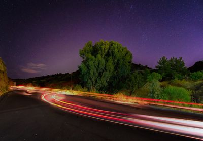 Light trails on road against clear sky at night