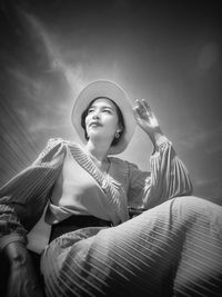 Low angle portrait of young woman against sky