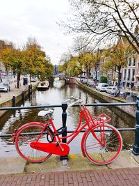 Bicycle parked by river in city against sky