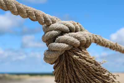 Close-up of rope tied on wooden post against sky