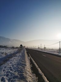 Road by snow covered mountain against clear sky