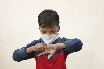 Close-up of boy wearing flu mask holding finger standing against wall
