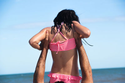 Cropped hand man holding girl mid air against sea