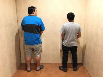 Rear view of men urinating in public bathroom