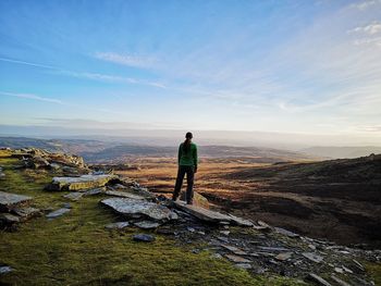 Rear view of man standing on rock against sky