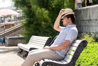 Side view of young man sitting on bench