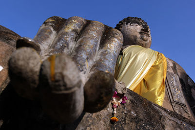 Low angle view of weathered buddha statue against clear sky