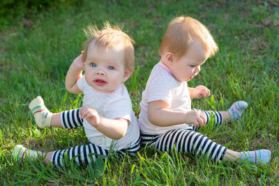 The twins are sitting on the green grass on sunny day in the city park.