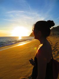 Woman looking at sea shore against sunset sky